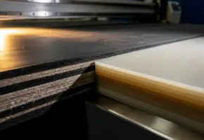 Stapel rubber, vilt en plastic platen op een precisie-snijmachine, één vel mid-snede met scherpe randen op tiende-millimeter nauwkeurigheid.