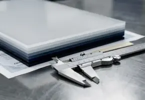 Gestapelde precisiegesneden kunststofplaten met certificeringsdocumenten en schuifmaat op stalen werktafel.