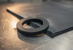Precisiegesneden rubberen pakking naast een ruw rubber vel met snijsporen op een roestvrijstalen werktafel.