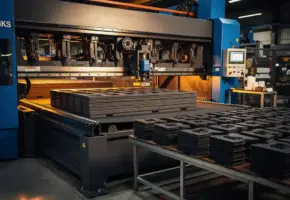 Industriële snijmachine in werking op fabriekshal, met precisiegesneden rubber en plastic onderdelen in nette rijen ernaast.