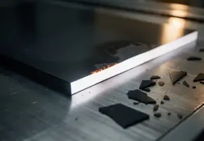 Donkere ABS kunststof plaat halverwege gesneden op industriële snijmachine, met witte doorsnede en kleine afvalstukjes, close-up.