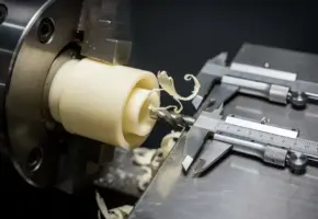 Precisie gedraaid kunststof onderdeel in roestvrijstalen klauwplaat, met krullende plastic spanen en micrometer op metalen werkbank.