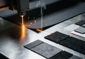 Industriële lasersnijder snijdt donker rubber met gloeiende amberkleurige laserstraal, rookpluim stijgt op boven precisiegesneden materiaalstalen.