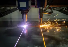 Laserkopsnijder en plasmabrander naast elkaar op donkere staalplaat, met violet-wit laserstraal en oranje plasmavonken.
