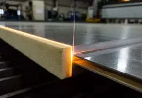 Laserstraal snijdt nauwkeurig door sandwichpaneel met schuimkern tussen metalen deklagen, gloeiende oranje snijrand met rookspoor.