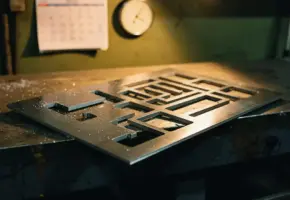 Verslaggeld staalplaat met geneste lasergestanste onderdelen op industriële werkbank, warm amberkleurig licht en metaalstof zichtbaar.