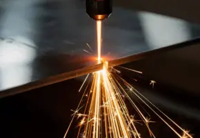 Laserstraal snijdt door roestvrijstalen plaat met spattende gesmolten vonken in donkere industriële werkplaats.