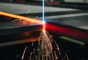Industriële lasersnijmachine snijdt door dik staalplaat met gloeiend oranje vonken en elektrisch blauw laserlicht.