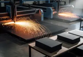 Lasersnijmachine in werking op fabriekshal, oranje vonken spatten over industrieel rubberplaat, tweede machine zichtbaar op achtergrond.