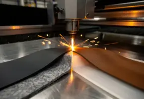 Precisie lasermachine snijdt door rubber, vilt, plastic en leer in waaierpatroon op stalen werkvlak, oranje vonken zichtbaar.